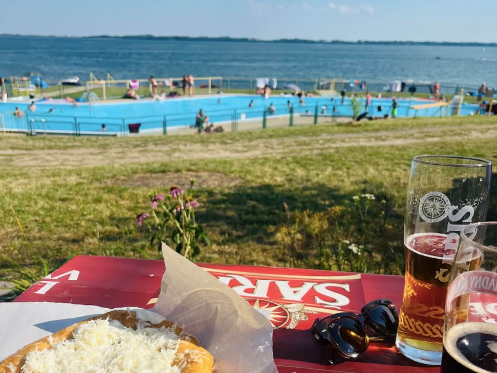Langoš s pivom na terase pri bazéne s ľuďmi na brehu jazera.